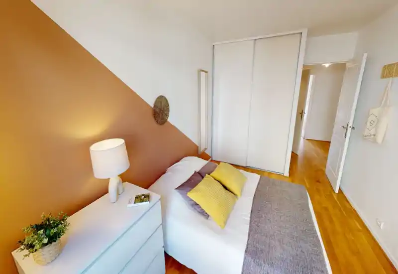 Chambre bien mise en scène avec un lit double confortable, un mur d'accent chaleureux, une lampe de chevet et une armoire intégrée ; lumineuse, cosy et prête à recevoir.