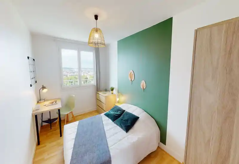 Chambre lumineuse et soignée avec un lit double devant un mur vert, lampes de chevet et un petit bureau près de la fenêtre — idéale pour un séjour cosy ou télétravail.