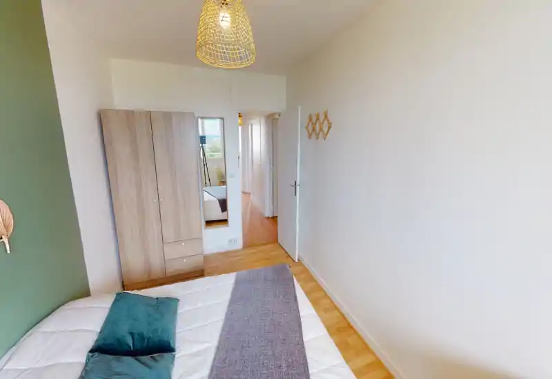 Chambre confortable avec un lit double en linge blanc, coussins bleu-vert et un jeté gris ; une armoire en bois et une glace en pied près de la porte, éclairage suspendu tressé apportant une ambiance chaleureuse.