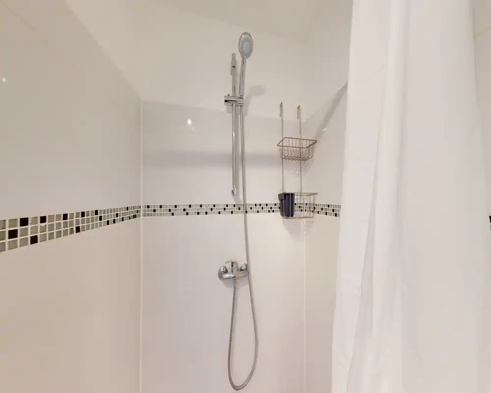 Cabine de douche moderne et propre avec douchette, carrelage et rideau blanc ; lumineux et bien entretenu.