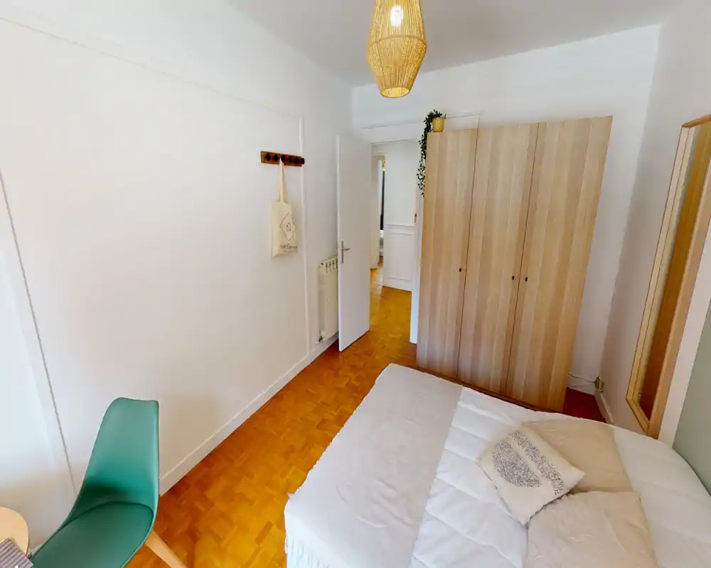 Chambre lumineuse et chaleureuse avec un lit double bien fait, une armoire en bois et un luminaire suspendu chaleureux. Parquet au sol et décoration minimaliste pour une ambiance apaisante.