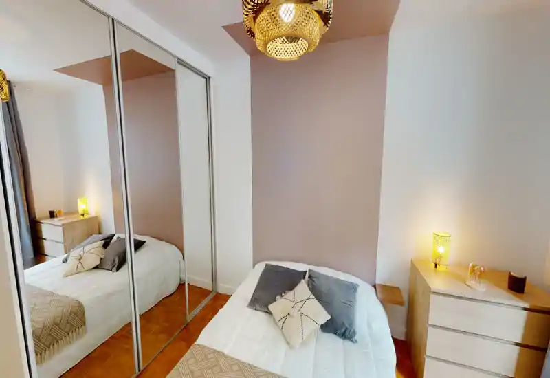 Bright, cozy bedroom with a neatly made double bed, decorative pillows, warm bedside lamps and a mirrored wardrobe that increases perceived space.