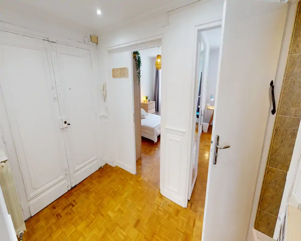 Bright entry hallway with parquet flooring, white paneled doors and visible access to adjacent bedroom and rooms — a clear, welcoming entrance area.