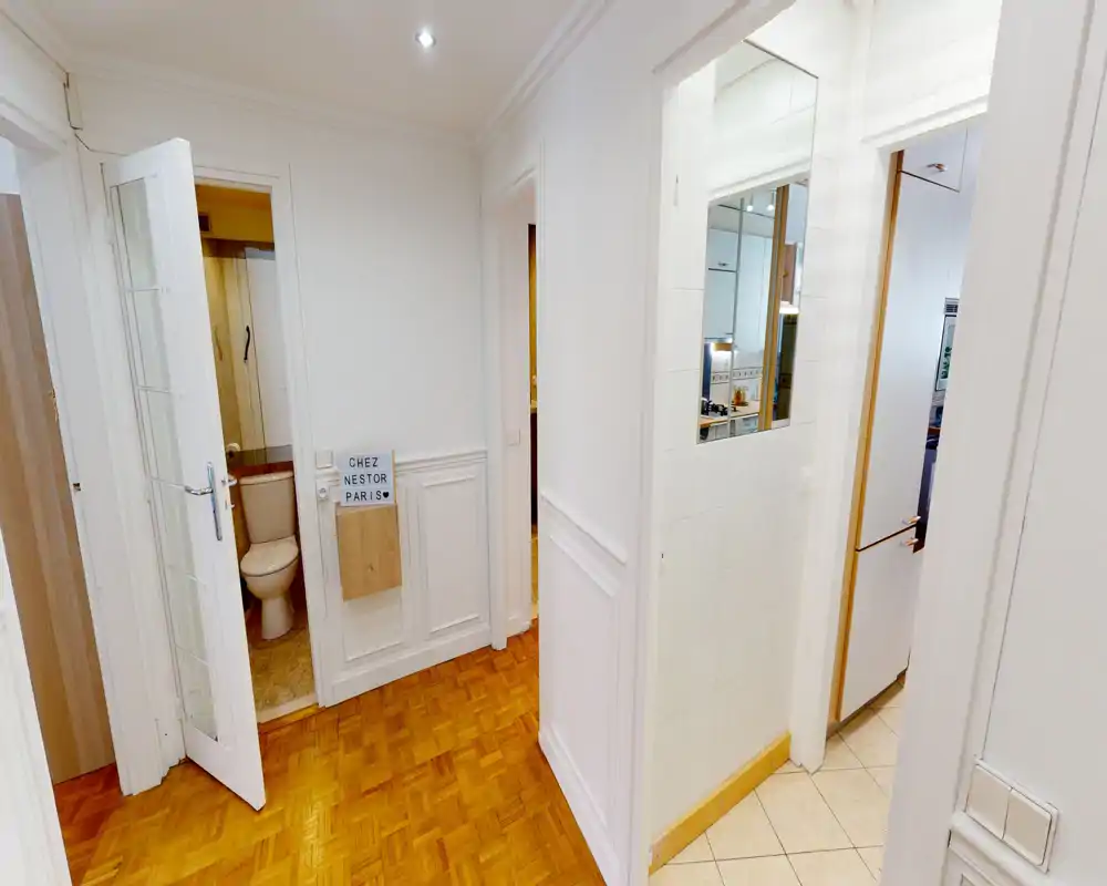 Bright, clean entrance hallway with parquet flooring, white paneled walls and doors leading to a bathroom and kitchen.