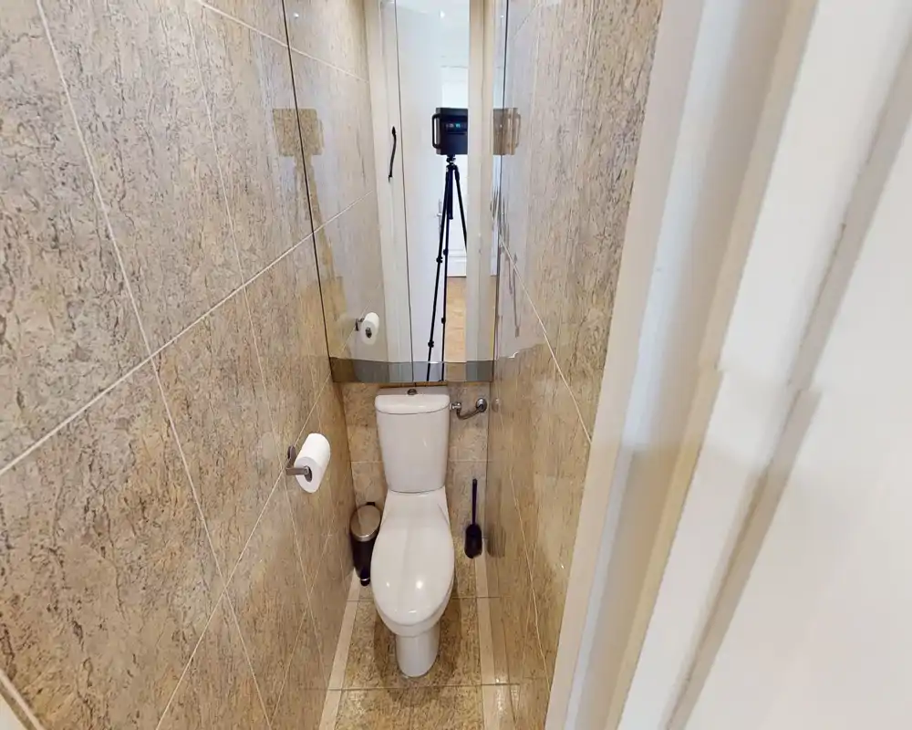 Compact, tiled bathroom with a floor-mounted toilet, wall-mounted mirror and compact accessories; bright, clean and well-lit.