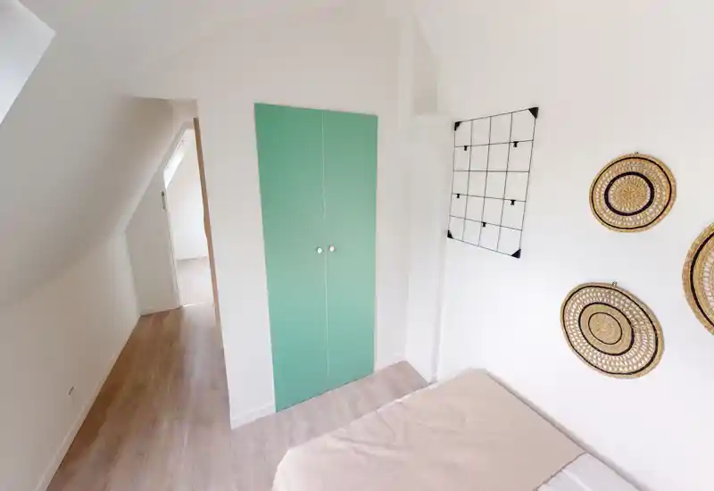 Bright attic bedroom with a partially visible bed, mint-green built-in closet and decorative wall baskets — simple, well-lit space ideal for a single occupant.