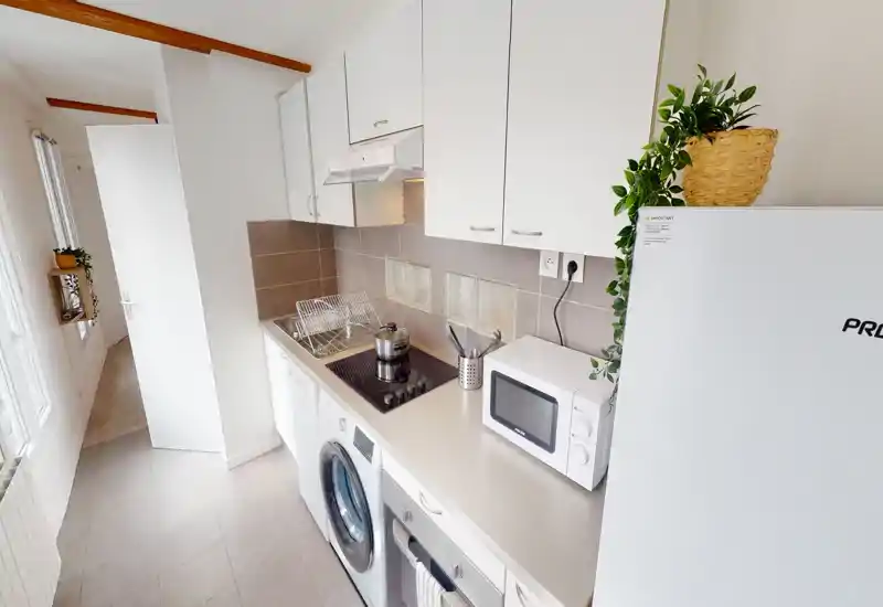Compact modern kitchen with built-in appliances, induction hob, microwave and washing machine; bright, tidy and well organized for efficient use.