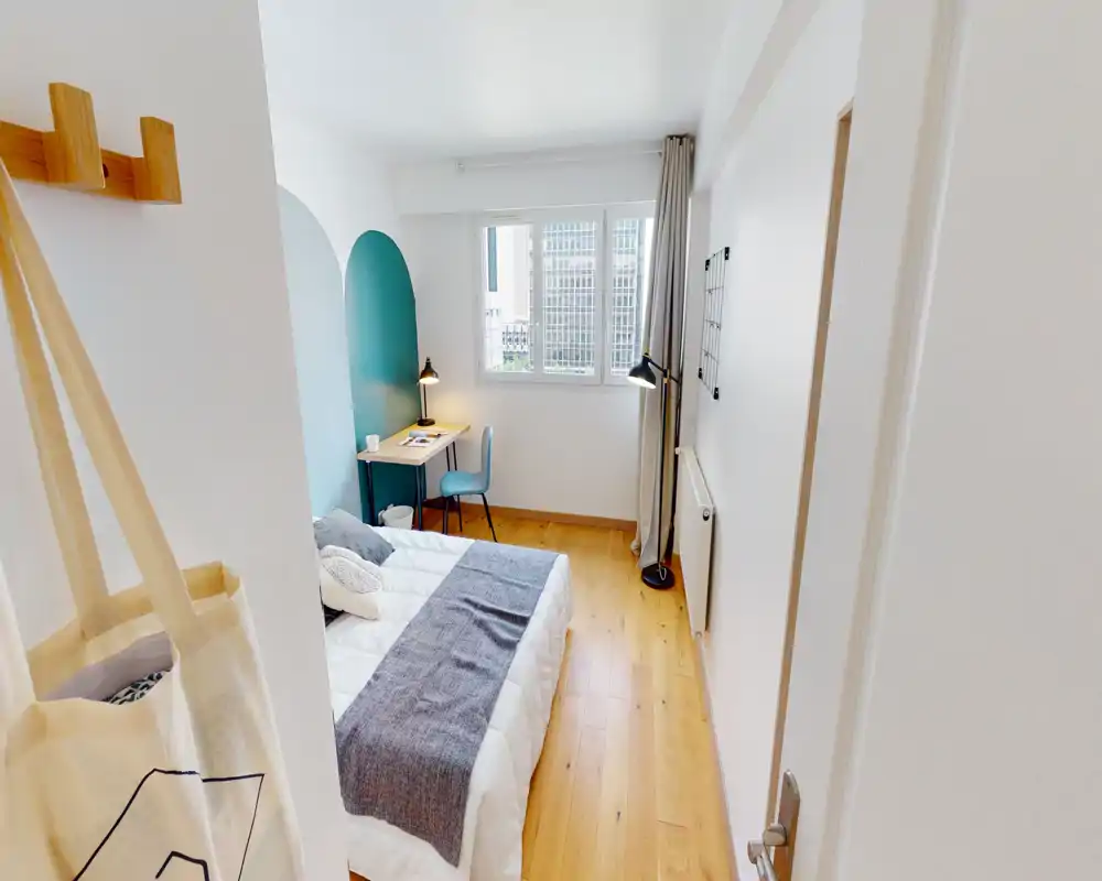 Camera da letto luminosa e moderna con letto matrimoniale ben rifatto, pavimento in legno e una piccola scrivania vicino alla finestra. La parete d'accento turchese e i tessili rendono l'ambiente accogliente e ben curato per gli affitti.