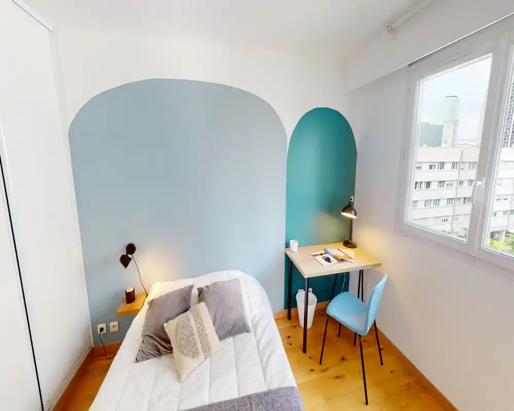 Camera da letto luminosa e compatta con letto ben rifatto, cuscini morbidi e una piccola scrivania vicino alla finestra. Le pareti con colori ad arco e l’illuminazione calda rendono lo spazio moderno e accogliente, perfetto per affitti brevi o studenti.
