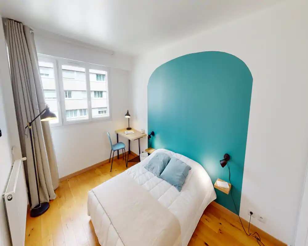Camera da letto moderna e luminosa con letto matrimoniale posizionato davanti a una parete accent color turchese. Ampia finestra, pavimento in legno e lampade da comodino creano un’atmosfera accogliente, perfetta per annunci.