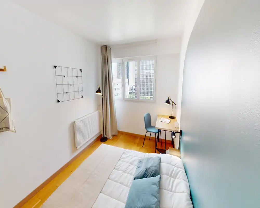 Camera da letto luminosa e ben messa in scena con letto matrimoniale, cuscini morbidi e una scrivania vicino alla finestra — ideale per soggiorni confortevoli o lavoro da casa.