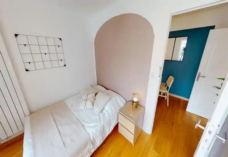 Compact, stylish single bedroom with a cozy arched feature wall, bedside table with lamp, soft bedding and warm wood floors—bright and well-staged for short-term rental photos.