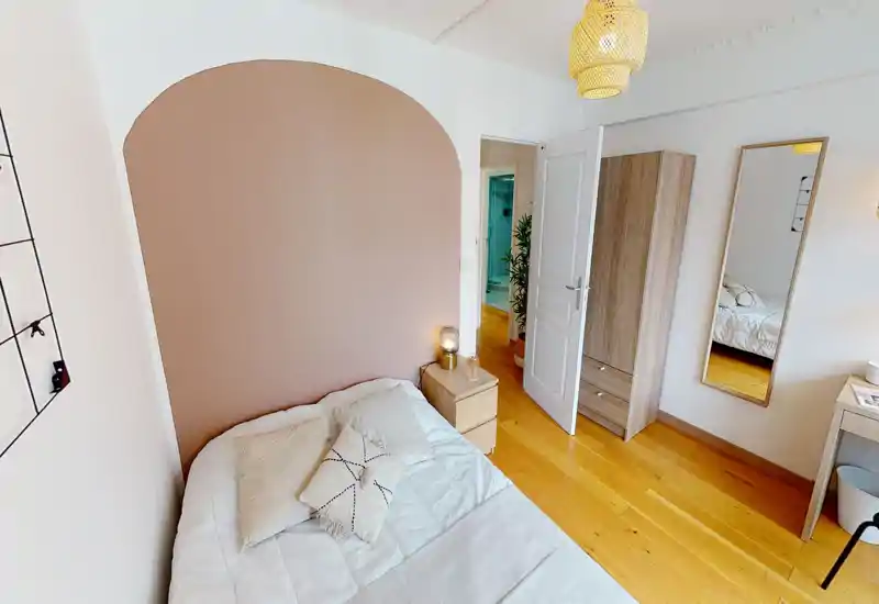 Bright, cozy bedroom with a double bed against a soft terracotta arched accent wall, bedside table with lamp, full-length mirror and light wood flooring.