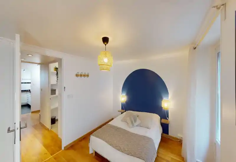 Bright, cozy bedroom with a double bed against a decorative blue arch headboard, warm wooden floors and soft bedside lighting.