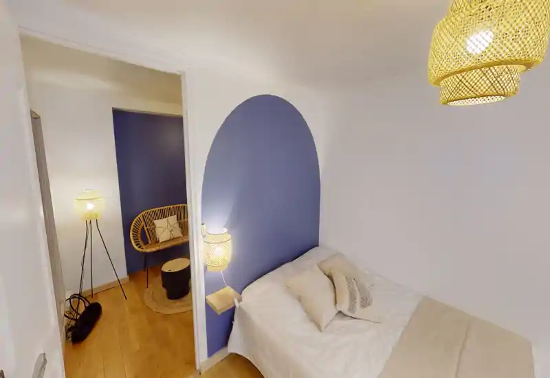 Cozy bedroom with a neatly made single/double bed against a soft blue arched accent wall, warm woven lighting and natural wood flooring for a welcoming atmosphere.