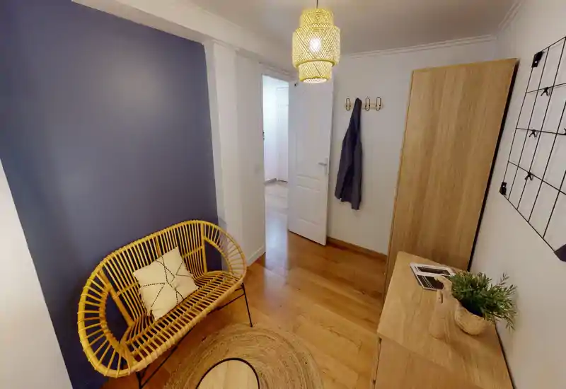 Bright, welcoming entrance/hallway with wooden flooring, a rattan bench, coat hooks and a slim cabinet — styled with a rug and pendant light.