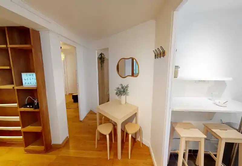 Compact, bright living/entry area with a small wooden table, three stools and warm hardwood floors — ideal for a cozy breakfast nook or compact dining.