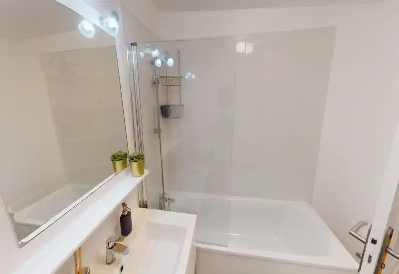 Clean, well-lit bathroom with a bathtub and glass shower screen, modern sink and mirror.