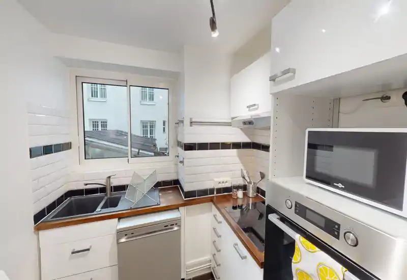 Compact modern kitchen with white cabinets, wooden countertops, built-in oven, microwave and an inset sink under a window — bright and neatly arranged for efficient use.