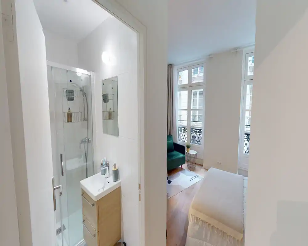 Dormitorio luminoso y acogedor con cama visible, grandes ventanas y una pequeña zona de estar; perfecto para anuncios que destaquen la luz natural y la comodidad.