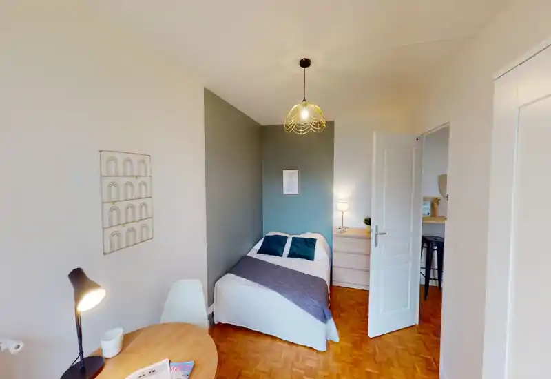 Compact, well-decorated bedroom with a double bed, bedside table and warm pendant lighting. The space feels bright and welcoming with coordinated textiles and a small workspace visible.