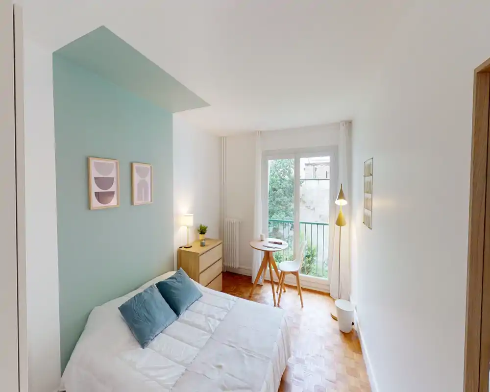 Camera da letto luminosa e di stile con letto matrimoniale, parete d'accento color verde acqua, comodino e un piccolo tavolo vicino alla finestra che regala molta luce naturale.
