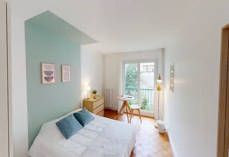 Camera da letto luminosa e di stile con letto matrimoniale, parete d'accento color verde acqua, comodino e un piccolo tavolo vicino alla finestra che regala molta luce naturale.