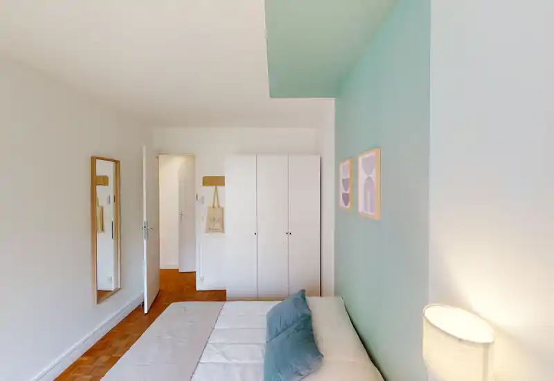 Camera da letto luminosa e ben arredata con un comodo letto matrimoniale, cuscini morbidi e una parete d'accento pastello; armadio e uno specchio a figura intera completano l'ambiente.