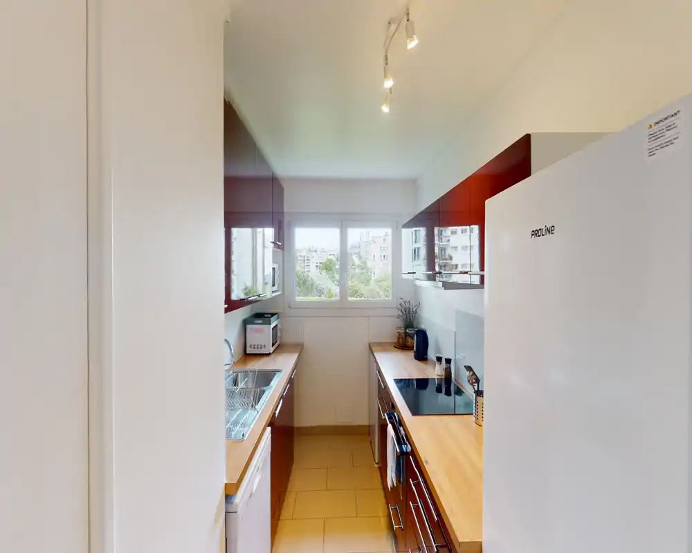 Bright galley kitchen with wooden countertops, glossy burgundy cabinets, integrated cooktop and a window providing natural light — compact and well organized for city living.