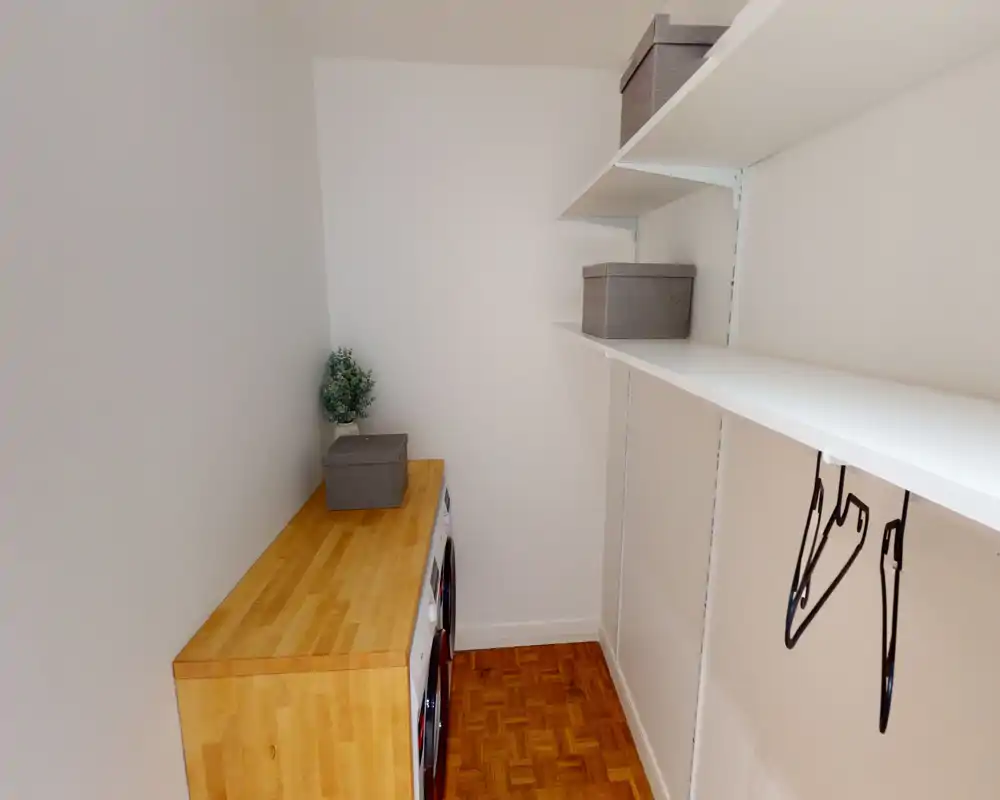 Small utility/entrance area with built-in shelving, a wooden countertop and stacked washer/dryer units; bright, clean and simply organized.