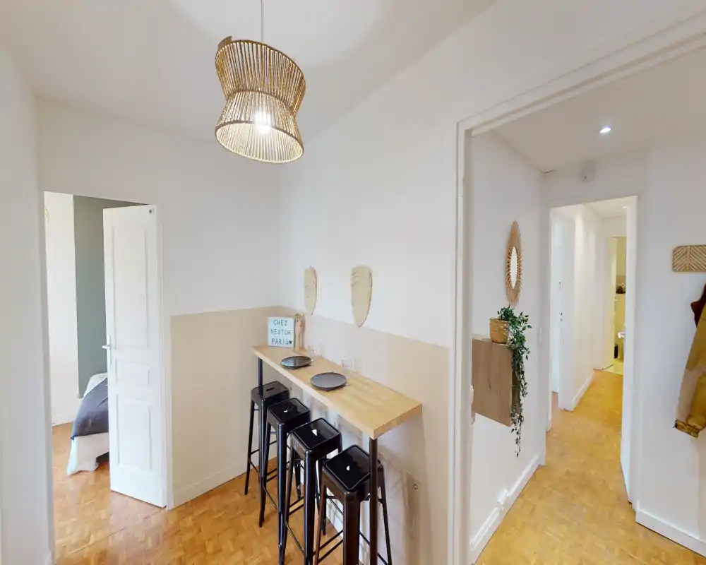 Compact dining/bar area with a wooden counter and three black stools, pendant light and warm parquet flooring — ideal for casual breakfasts or quick meals.