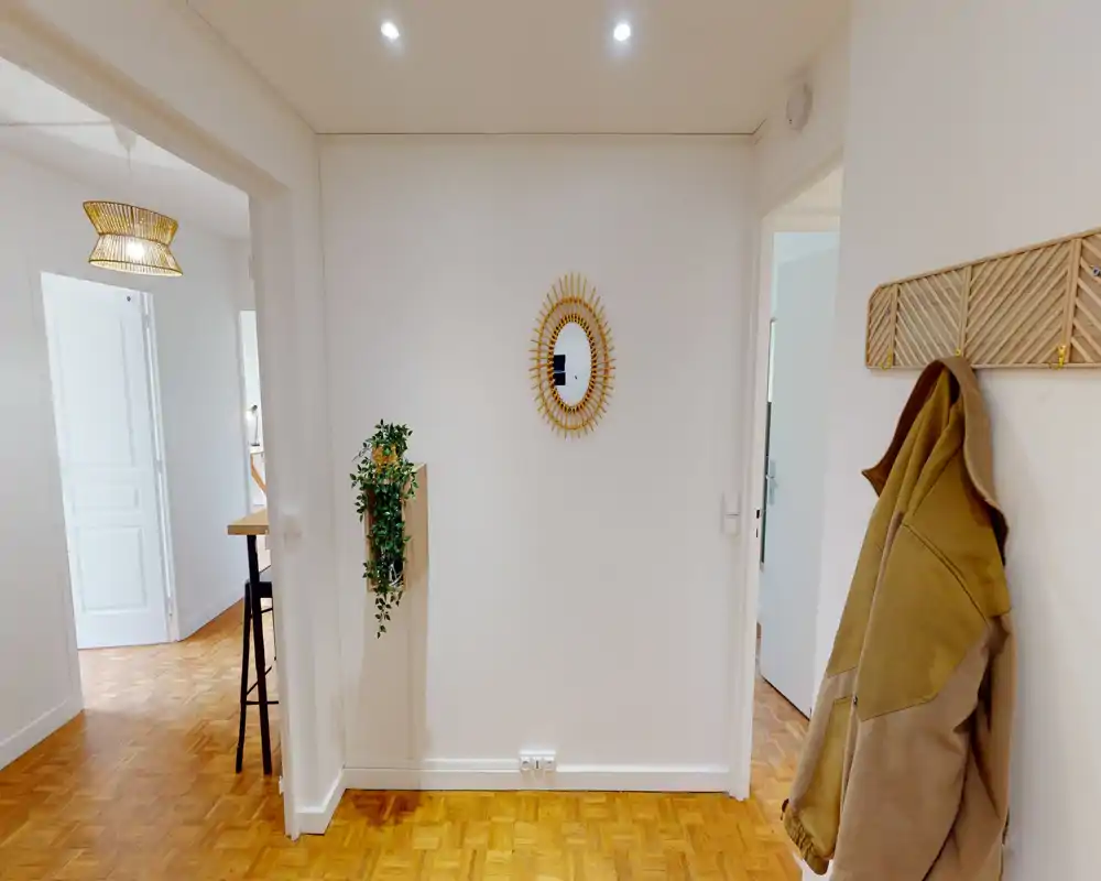 Bright, tidy entry hallway with parquet flooring, wall mirror and coat hooks — a welcoming entrance area that connects to adjacent rooms.