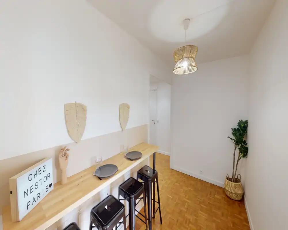 Small dining/breakfast area with a wooden counter, three metal stools and minimalist decor; bright, clean space suitable for casual meals.