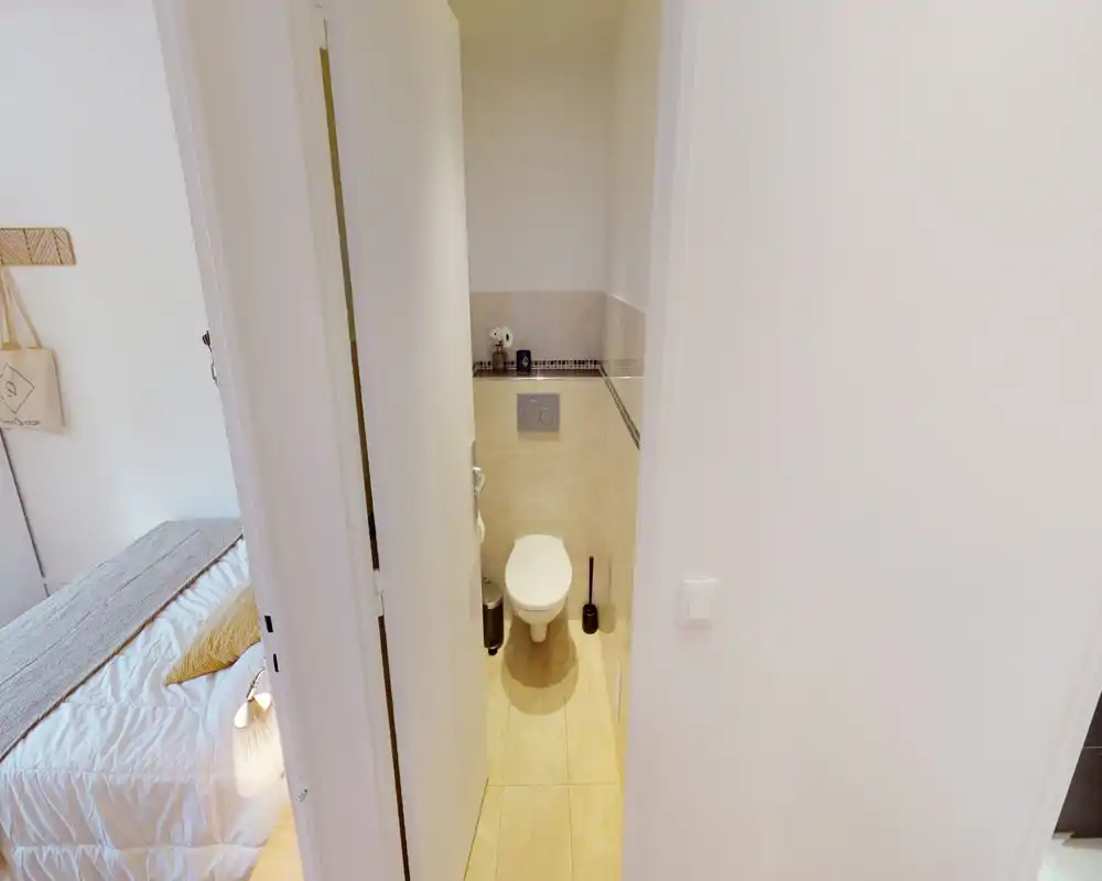 Compact private bathroom with wall-mounted toilet, tiled floor and neutral tones; bright and clean space suitable for a rental listing.
