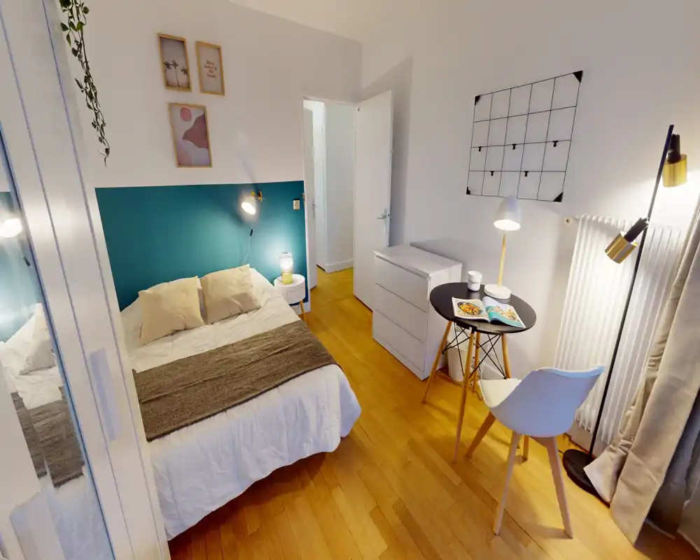 Chambre lumineuse et chaleureuse avec un lit double devant un mur d'accent bleu-vert, lampes de chevet, petit bureau et chaise, et parquet clair — idéale pour des annonces mettant en avant confort et style moderne.