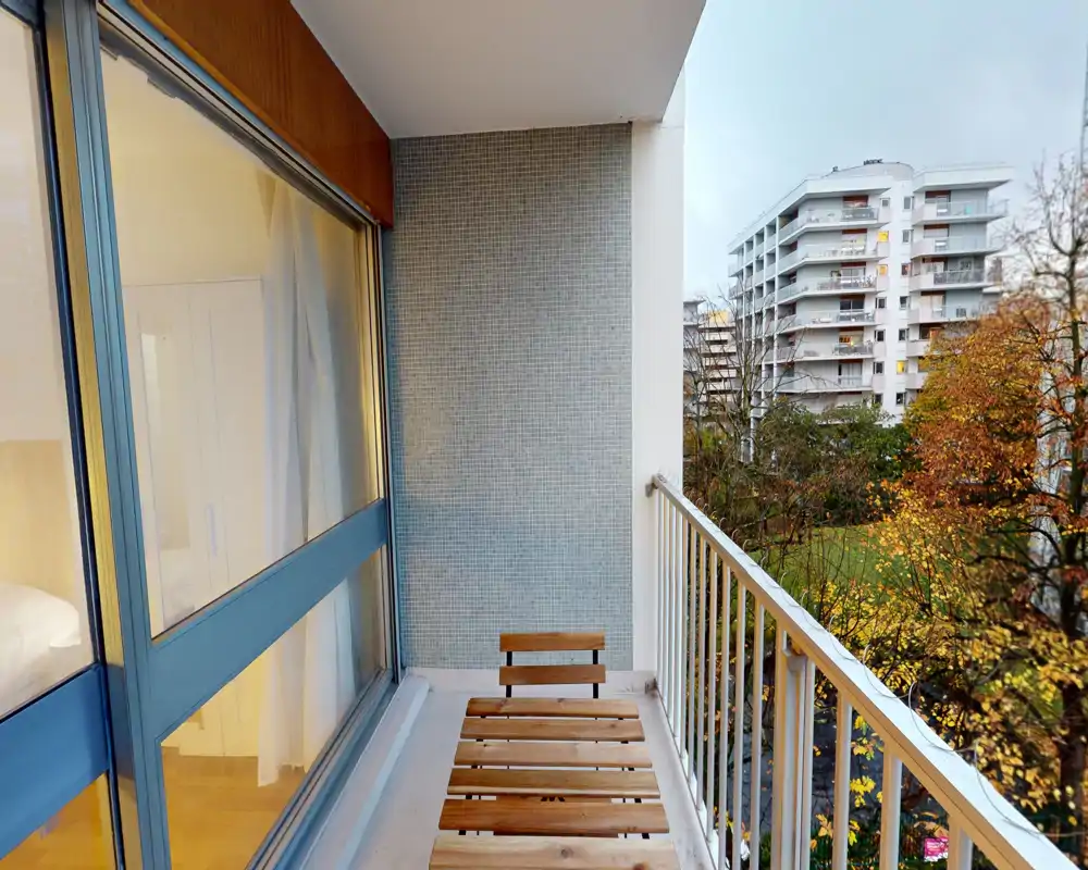 Petit balcon privé avec assise en lattes de bois et vue sur des arbres et des immeubles voisins — idéal pour le café du matin.