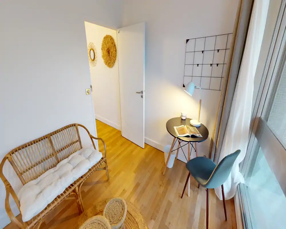Espace de vie lumineux et élégant avec assise en rotin, petite table et chaise près d’une grande fenêtre — parquet chaleureux et décorations douces pour une ambiance cosy et moderne.