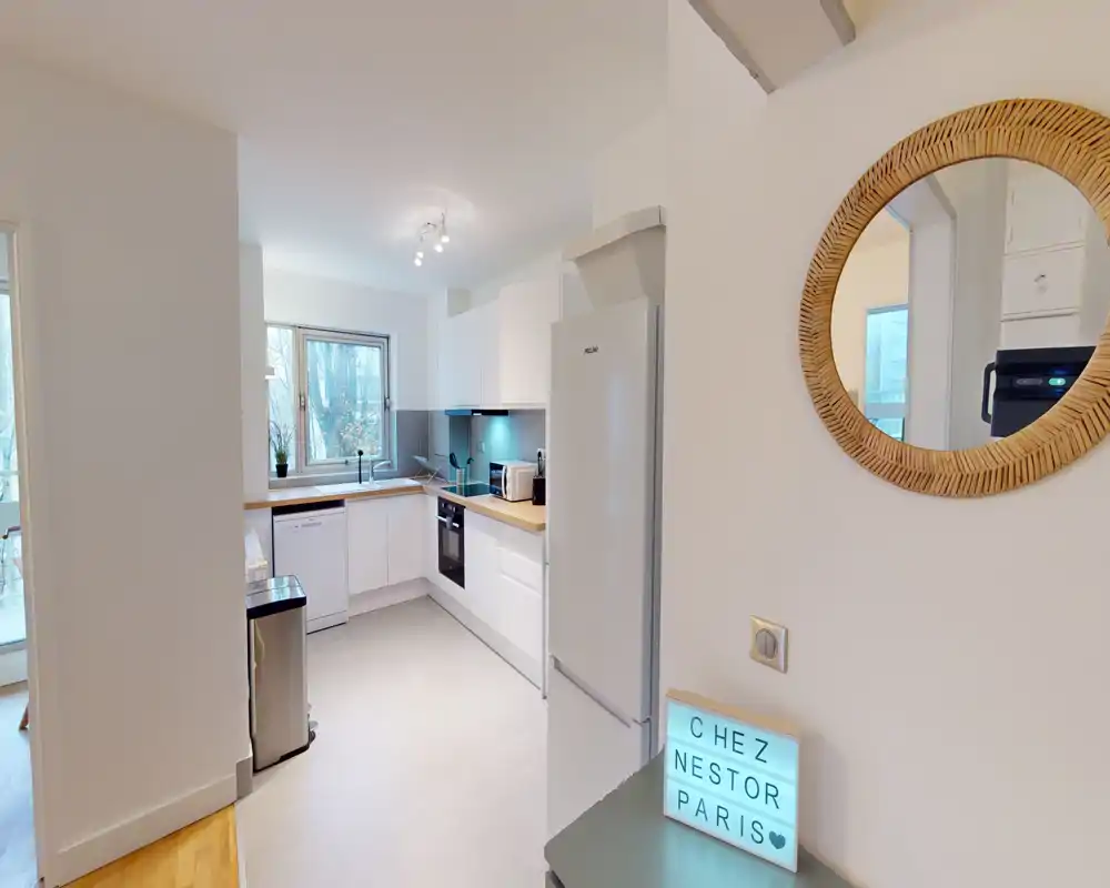 Cuisine moderne et lumineuse avec placards blancs, plans de travail en bois et électroménagers intégrés ; fenêtre apportant une belle lumière naturelle.