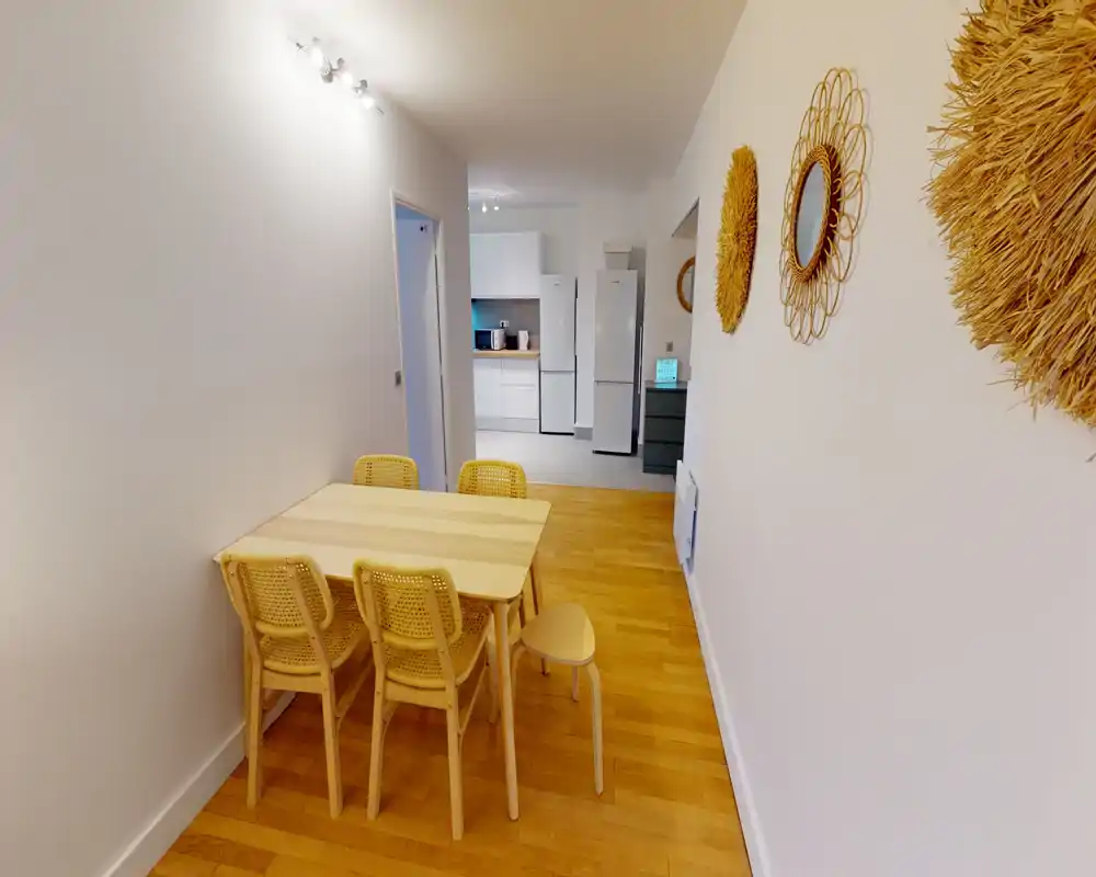 Coin repas lumineux et compact avec une table en bois clair et quatre chaises assorties, parquet chaleureux et miroirs muraux décoratifs qui apportent du charme.