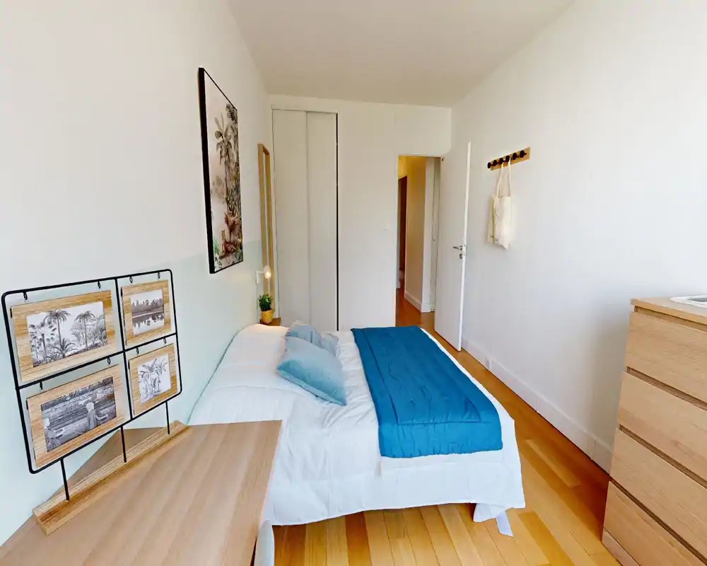Chambre lumineuse et bien mise en scène avec un lit double en linge blanc et jeté bleu ; sol en bois et décoration minimaliste pour une ambiance moderne et apaisante.