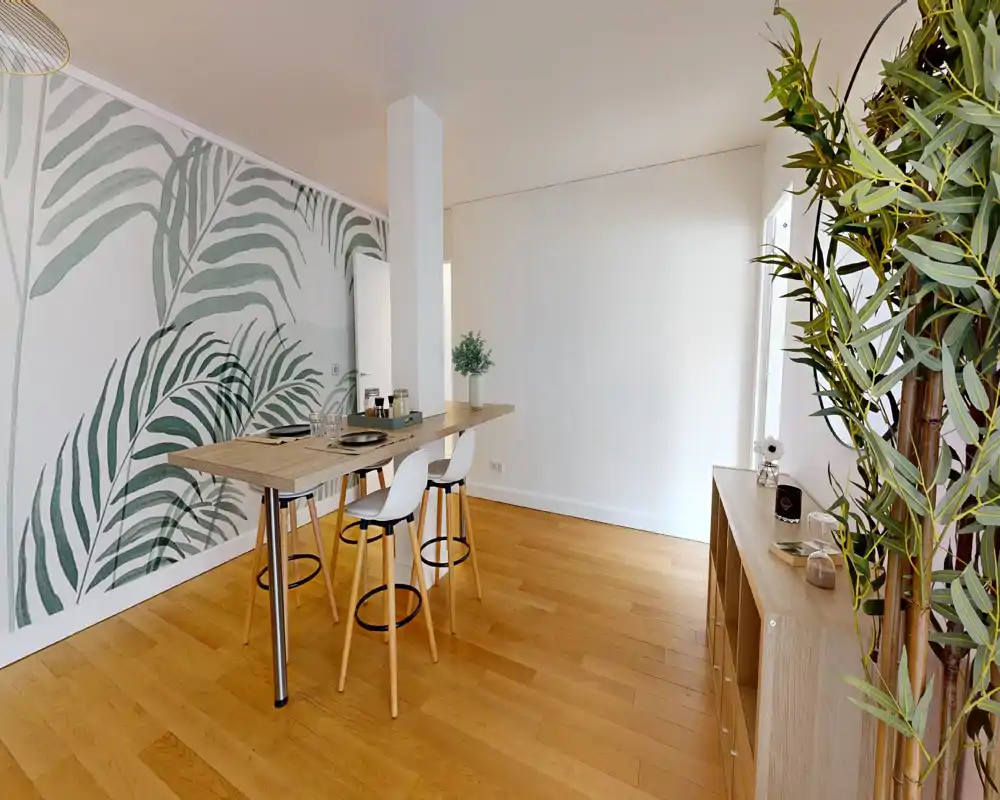 Espace repas lumineux et moderne avec table haute en bois, tabourets et papier peint botanique pour une ambiance fraîche et accueillante.