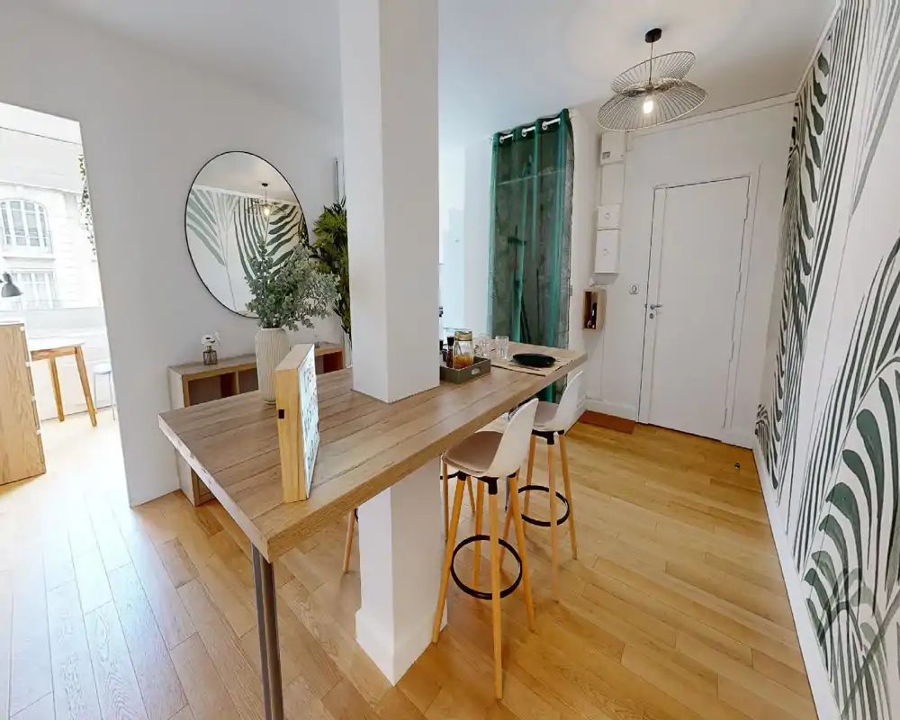 Espace de vie lumineux et moderne avec bar en bois, tabourets hauts, plantes décoratives et papier peint à motif ; lumière naturelle et parquet chaleureux créent une ambiance accueillante.