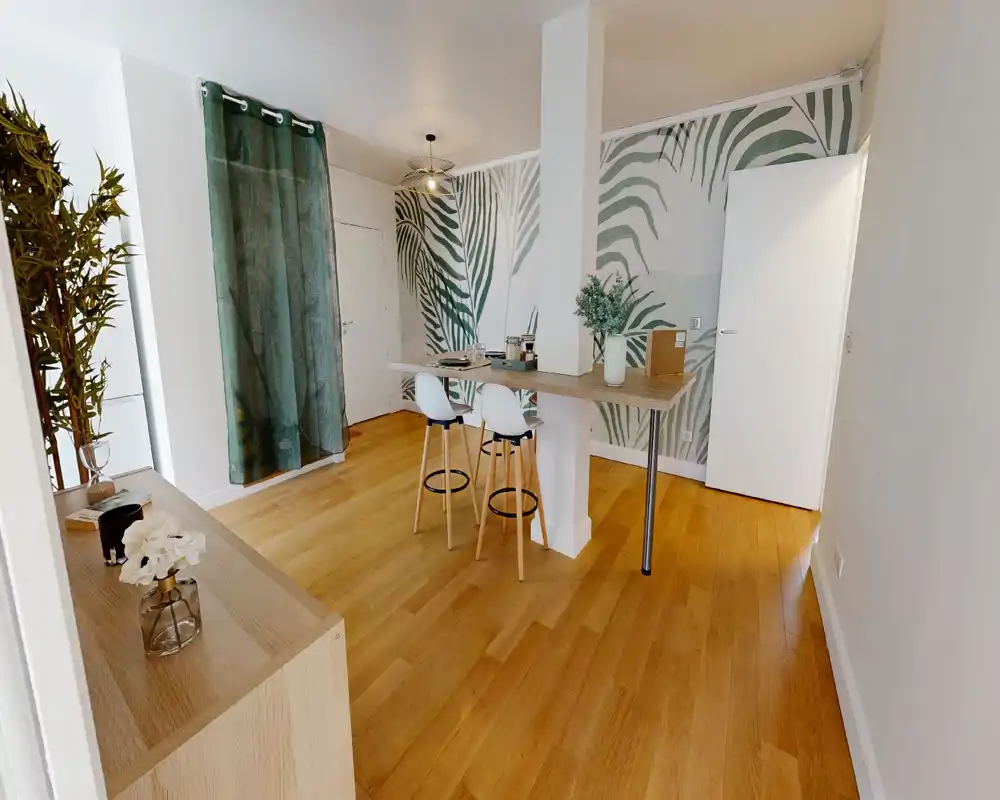 Espace repas lumineux et design avec bar petit-déjeuner et deux tabourets, papier peint à feuilles tropicales et parquet — parfait pour repas décontractés ou télétravail.