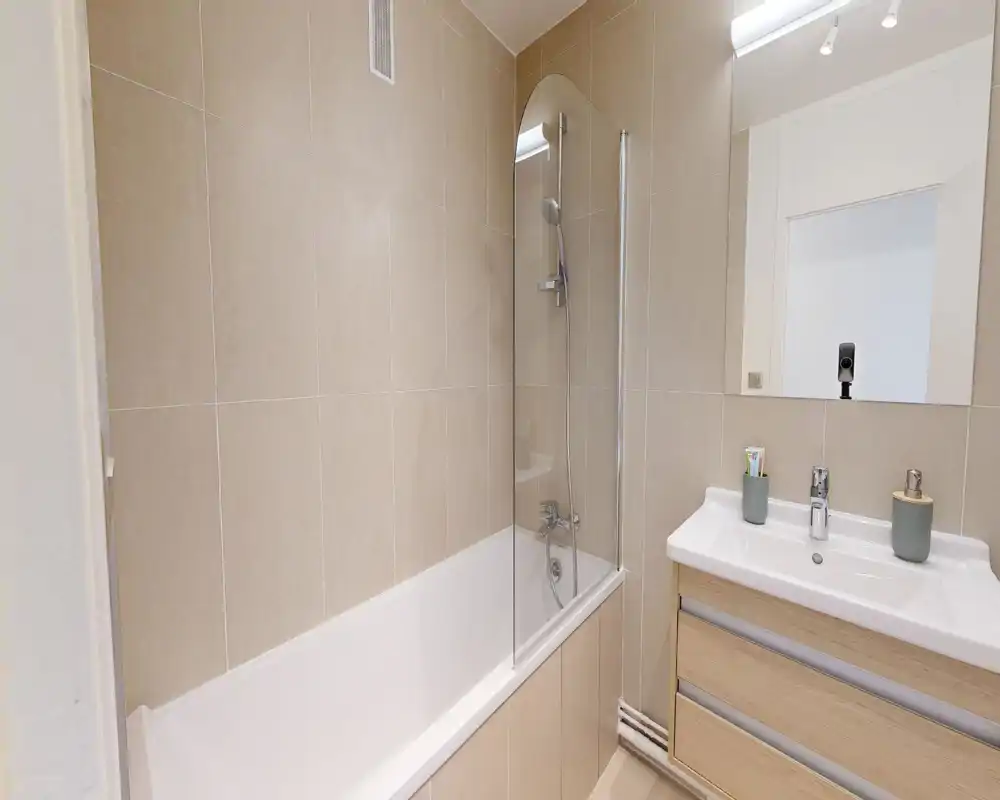 Salle de bains moderne et propre avec baignoire et paroi de douche, miroir mural et meuble lavabo avec tiroirs de rangement.