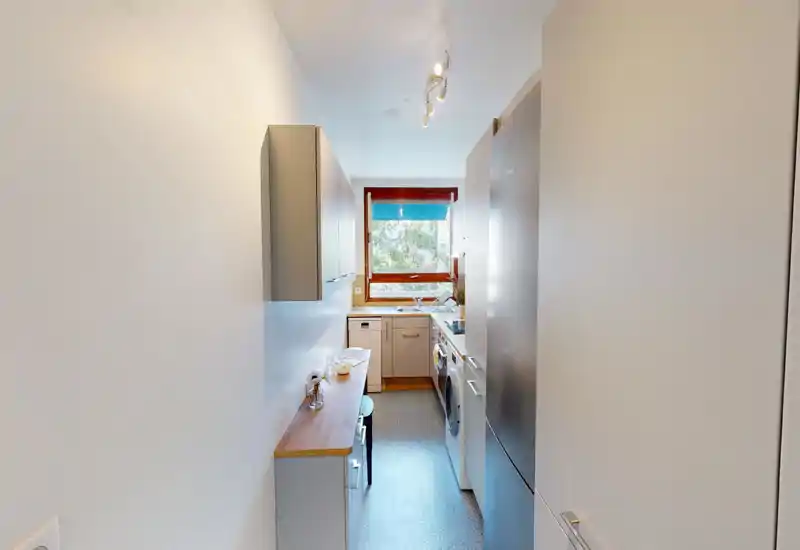 Cuisine moderne et étroite avec plans de travail en bois, appareils intégrés et une fenêtre apportant de la lumière naturelle. Agencement compact adapté à une utilisation efficace.