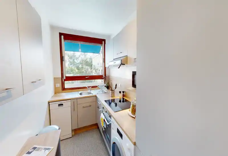 Cuisine compacte et moderne avec plans de travail en bois, électroménagers intégrés et une grande fenêtre offrant une belle luminosité — idéale pour un petit appartement.