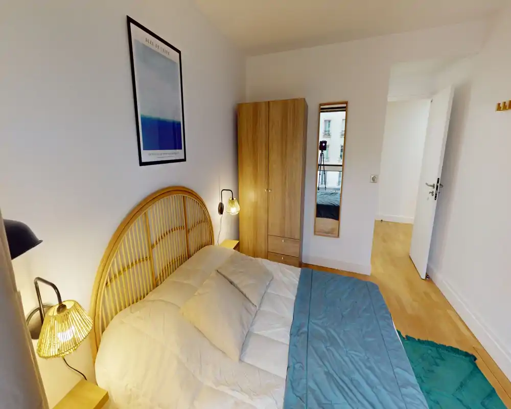 Chambre lumineuse et chaleureuse avec lit double, tête de lit en rotin, lampes de chevet et armoire; parquet et textiles apportent une ambiance accueillante.
