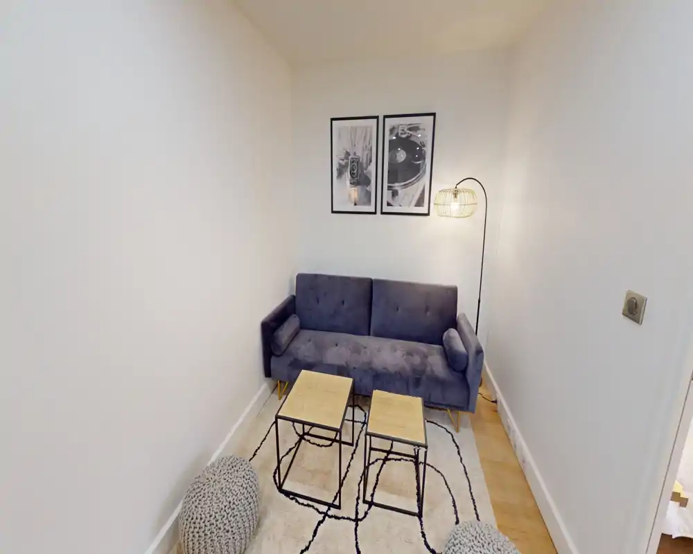Small, cozy living area with a plush two-seater sofa, patterned rug, two nesting coffee tables and warm floor lamp — ideal for relaxing in a compact space.