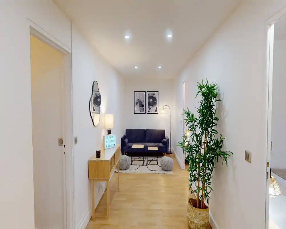 Well-styled small living area visible from the hallway: a compact sofa, coffee tables, poufs and warm lighting create a cozy sitting corner ideal for relaxing.