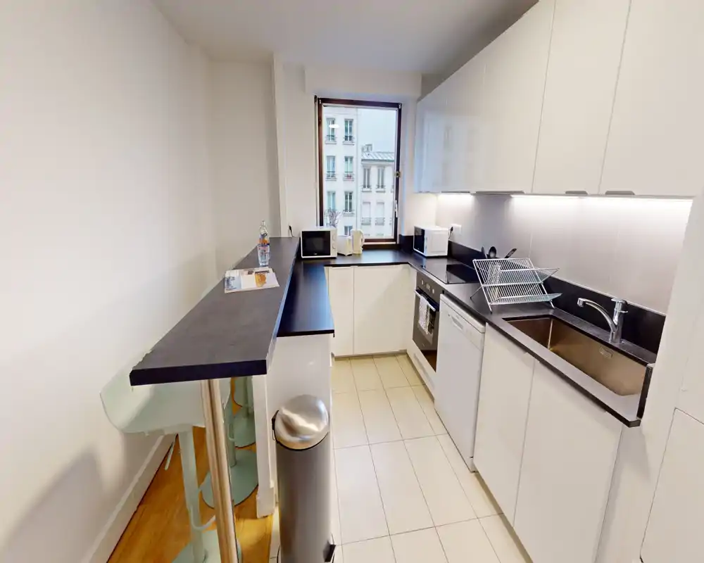 Bright, modern galley kitchen with integrated appliances, a stainless sink, under-cabinet lighting and a small breakfast bar by the window.
